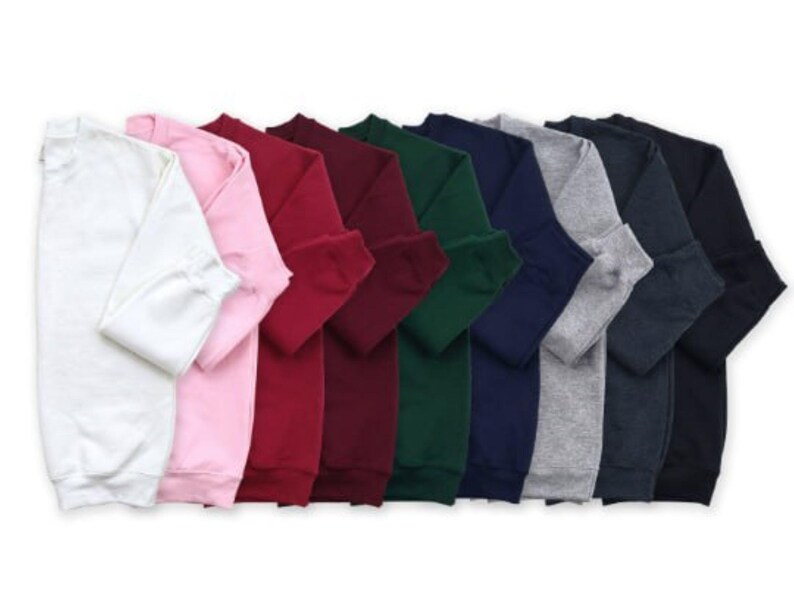 Op de afbeelding: Een verzameling sweatshirts met lange mouwen en een ronde hals in verschillende kleuren: wit, roze, rood, bordeaux, groen, marineblauw, grijs en zwart. De sweatshirts zijn opgevouwen en tonen de beschikbare tinten.