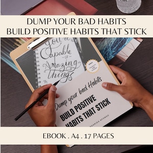 May include: A white and gray notebook with the text "Dump your bad habits, Build positive habits that stick" on the cover. The notebook is open to a page with the text "You're capable of amazing things" written in cursive. The notebook is on a clipboard with a wooden frame.