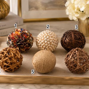 Pode incluir: Seis esferas decorativas numeradas de 1 a 6. A esfera 1 é multicolorida com pétalas em camadas. A esfera 2 é coberta por pequenas contas creme. A esfera 3 é de madeira trançada castanho-escura. A esfera 4 é de galhos castanho-claros. A esfera 5 é envolta em corda bege. A esfera 6 é de madeira trançada castanho-média.
