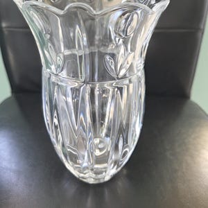 May include: A clear glass vase with a scalloped rim and leaf design. The vase has vertical ridges and a bulbous base. The glass reflects light, creating a sparkling effect. The vase is likely used for displaying flowers or as a decorative item.