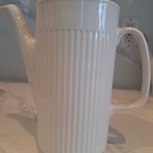 May include: White ceramic coffee pot with a ribbed design and a lid. The pot has a handle and a spout.