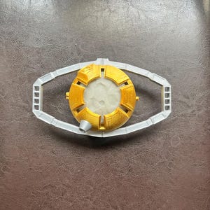 May include: A gold-colored, 3D printed, spherical object with a white center and a silver-colored frame. The object is designed to resemble a futuristic device.