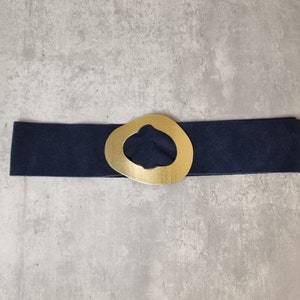 May include: A navy blue belt with a gold-colored, abstract-shaped buckle.