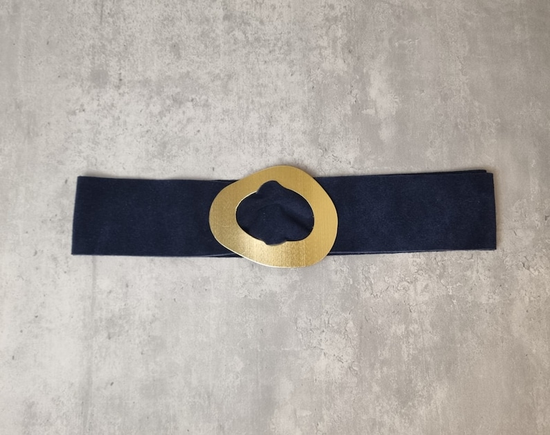 May include: A navy blue belt with a gold-colored, abstract-shaped buckle.