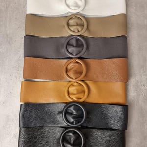May include: A set of eight leather belts with a round buckle. The belts are in various colors, including white, brown, gray, tan, and black.
