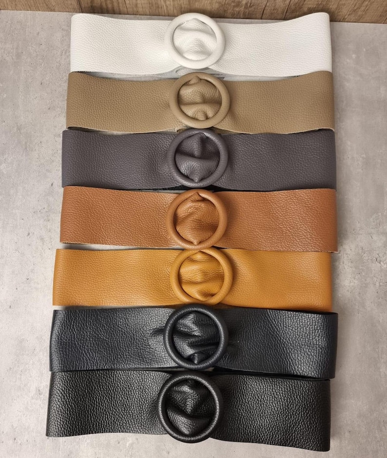 May include: A set of eight leather belts with a round buckle. The belts are in various colors, including white, brown, gray, tan, and black.