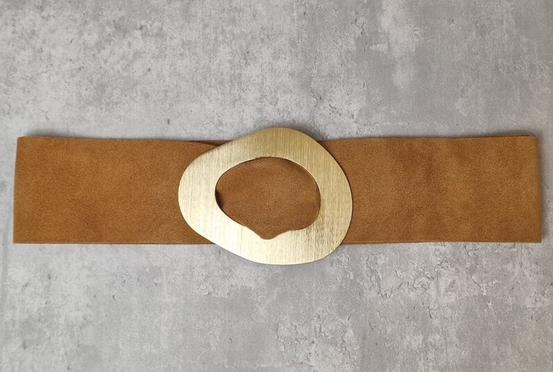 May include: A brown suede belt with a large, gold, oval-shaped buckle.