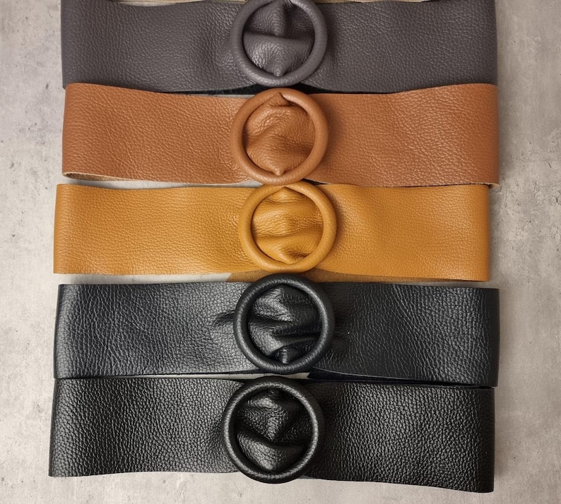 May include: Four leather belts with round, oversized buckles. The belts are in different colors: brown, tan, black, and dark gray.