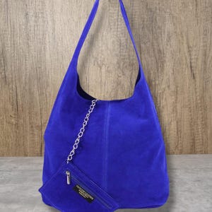 Könnte beinhalten: Eine hellblaue Umhängetasche aus Wildleder mit einem silbernen Kettendetail und einer kleinen passenden Tasche mit der Aufschrift "Genuine Leather".