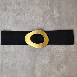 May include: A black leather belt with a gold-toned oval buckle. The buckle has a large, open circle in the center.
