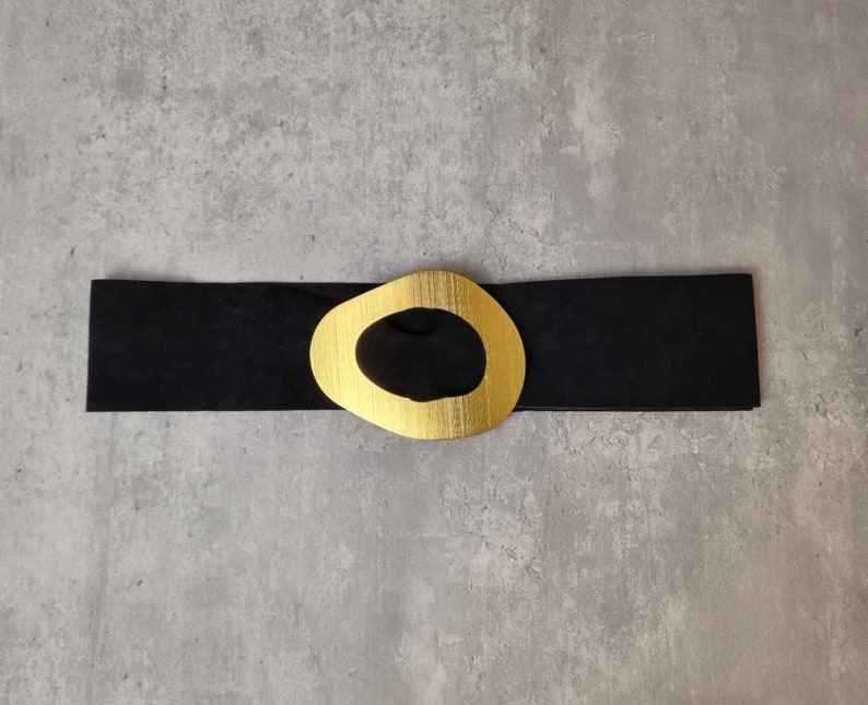 May include: A black leather belt with a gold-toned oval buckle. The buckle has a large, open circle in the center.