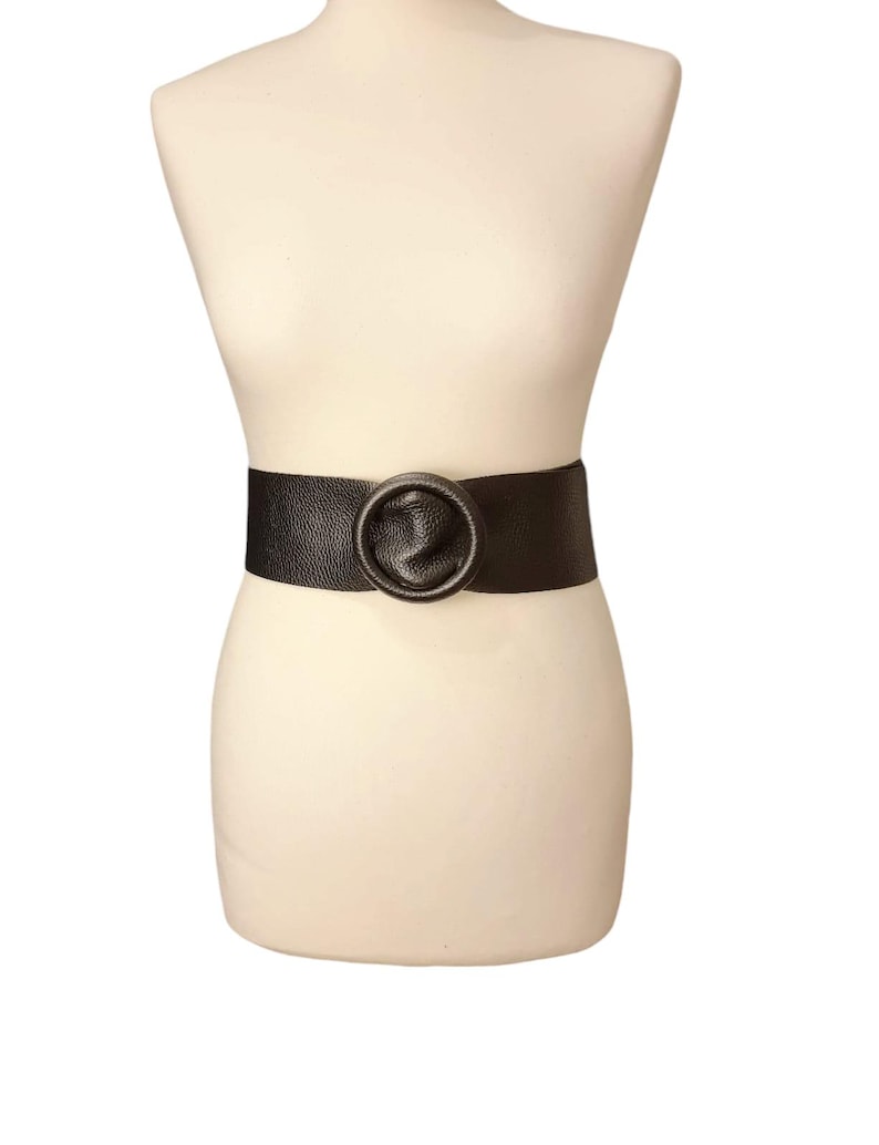 May include: A wide black leather belt with a large, round, textured buckle.