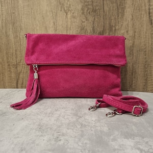 May include: A bright pink suede clutch bag with a long tassel and a detachable strap.
