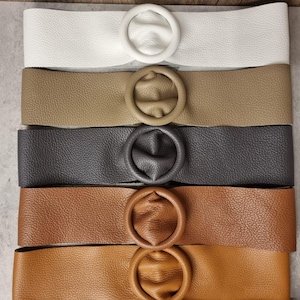 May include: Five leather belts with round metal buckles in different colors: white, beige, gray, brown, and tan.