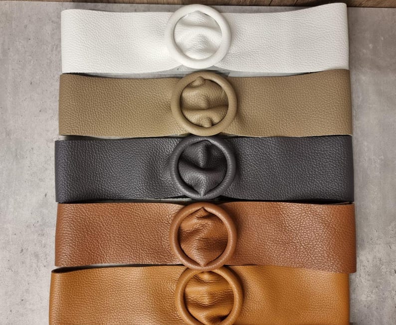 May include: Five leather belts with round metal buckles in different colors: white, beige, gray, brown, and tan.