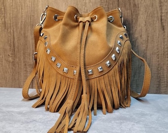 May include: A brown suede bucket bag with silver studs and fringe detailing. The bag has a drawstring closure and a long strap.