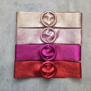 May include: Four leather belts with a large, round, metallic buckle in different colours: gold, pink, magenta, and red.