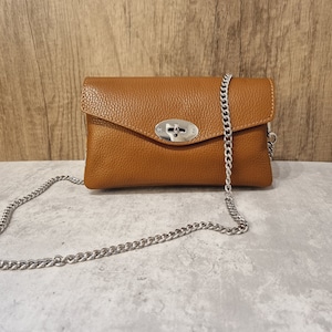 Puede incluir: Un bolso de hombro de cuero marrón con una correa de cadena plateada y un cierre de cierre plateado.