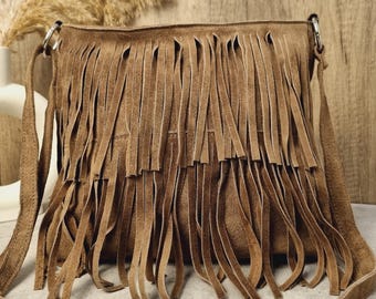 May include: A brown suede shoulder bag with long fringe detailing. The bag has a long, adjustable strap and silver-tone hardware. The fringe covers the front of the bag, creating a bohemian style.