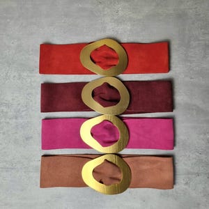 Peut inclure: Quatre ceintures en daim avec une grande boucle ovale dorée. Les ceintures sont dans des tons de rouge, bordeaux, rose et marron.