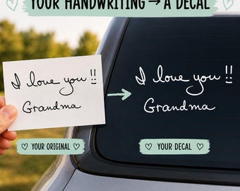 May include: A custom decal on a car window featuring the white text I love you!! Grandma, replicated from a handwritten note. The image displays the original black ink handwriting on white paper next to the white vinyl decal on the glass.
