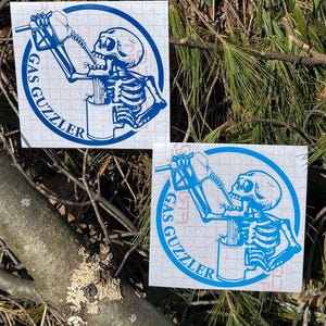 May include: Two square vinyl decals featuring a blue graphic of a skeleton drinking from a gas pump nozzle into a mug. The design is enclosed in a circular border with the text GAS GUZZLER printed along the bottom curve of the circle.