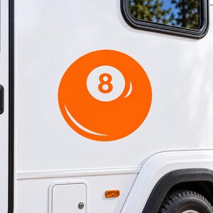 May include: A bright orange circular decal featuring a white number eight in the center, designed to resemble a billiard ball. The graphic is applied to the smooth white exterior side panel of a vehicle, positioned near a black window frame.