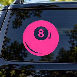 May include: A circular vinyl decal featuring a bright pink billiard ball design with a dark navy blue center circle containing the number eight in pink. The graphic includes a curved highlight line on the lower left and a curved shadow on the right.