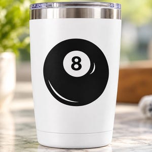 May include: A white stainless steel tumbler featuring a black graphic of an eight ball on the front. The drinkware has a tapered cylindrical shape with a metallic silver rim at the top and a clear lid, showcasing a clean and simple design.