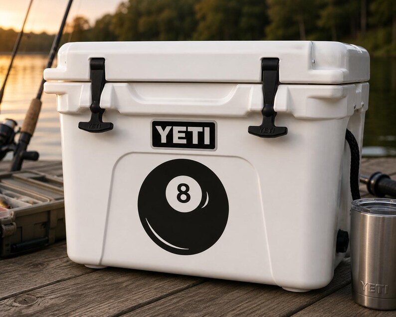 May include: A white YETI cooler featuring a black and white 8-ball graphic on the front. The rectangular cooler has two black rubber T-latches on the lid and the YETI brand name printed in white letters on a black rectangular background.