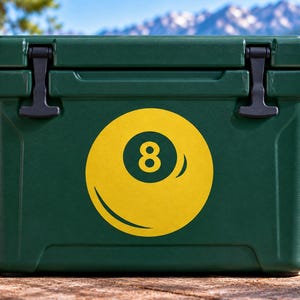 May include: A dark green rectangular cooler featuring a large yellow graphic of an eight ball on the front center. The cooler has a solid lid with two black rubber latches on the top corners and a smooth, durable exterior finish for storage.
