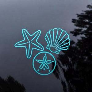 Puede incluir: Un adhesivo de vinilo azul claro que muestra una estrella de mar de cinco puntas, una concha de abanico y un dólar de arena circular con un patrón de estrella central. El diseño está compuesto por líneas limpias y continuas sobre vidrio.