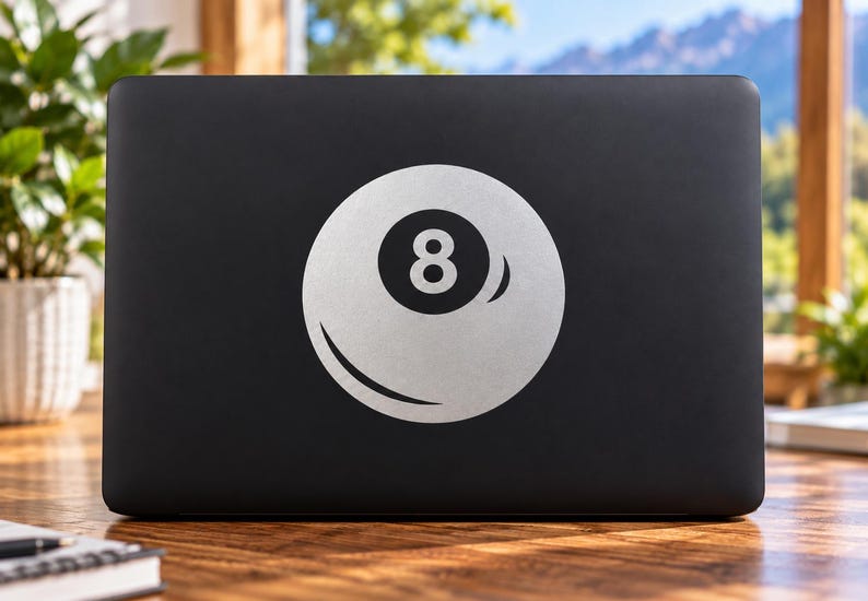 May include: A matte black laptop featuring a large, centered white graphic of a billiard eight ball. The circular design displays the number eight in a bold black font within a white circle, accented by a curved white highlight on the lower edge.