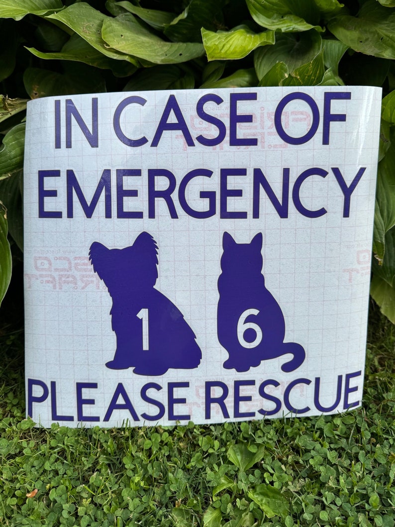 May include: A white sign with dark blue text and graphics. The text reads "IN CASE OF EMERGENCY PLEASE RESCUE." Silhouettes of a dog and cat are featured, with the numbers "1" and "6" inside. The sign is placed on grass.