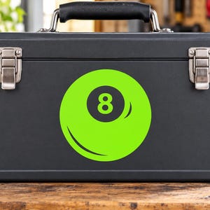May include: A matte black rectangular metal toolbox featuring a prominent lime green circular decal on the front. The decal displays a stylized black number eight inside a dark circle, mimicking the appearance of a billiard ball design.