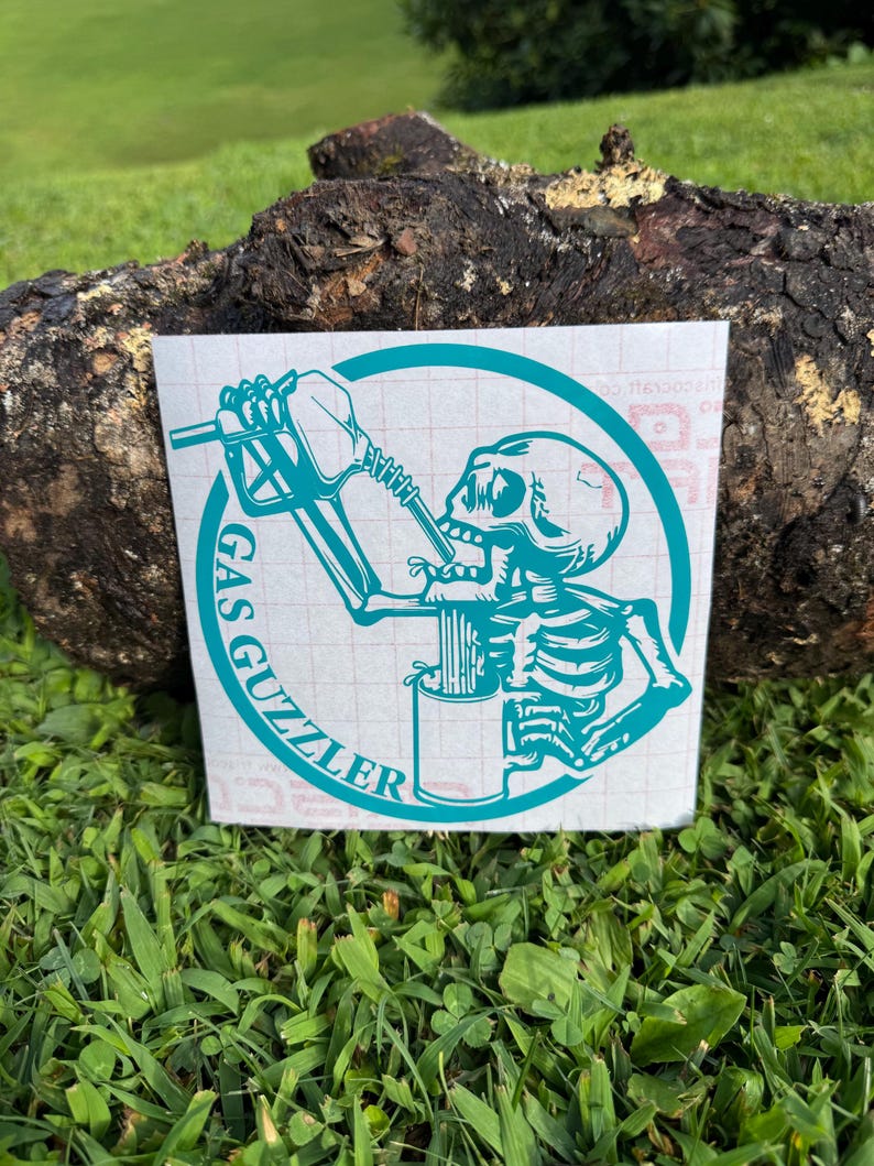 May include: A teal-colored vinyl decal featuring a skeleton drinking from a gas pump nozzle into a mug, enclosed within a circular border. The text GAS GUZZLER is printed in a bold, sans-serif font along the left side of the circular frame.