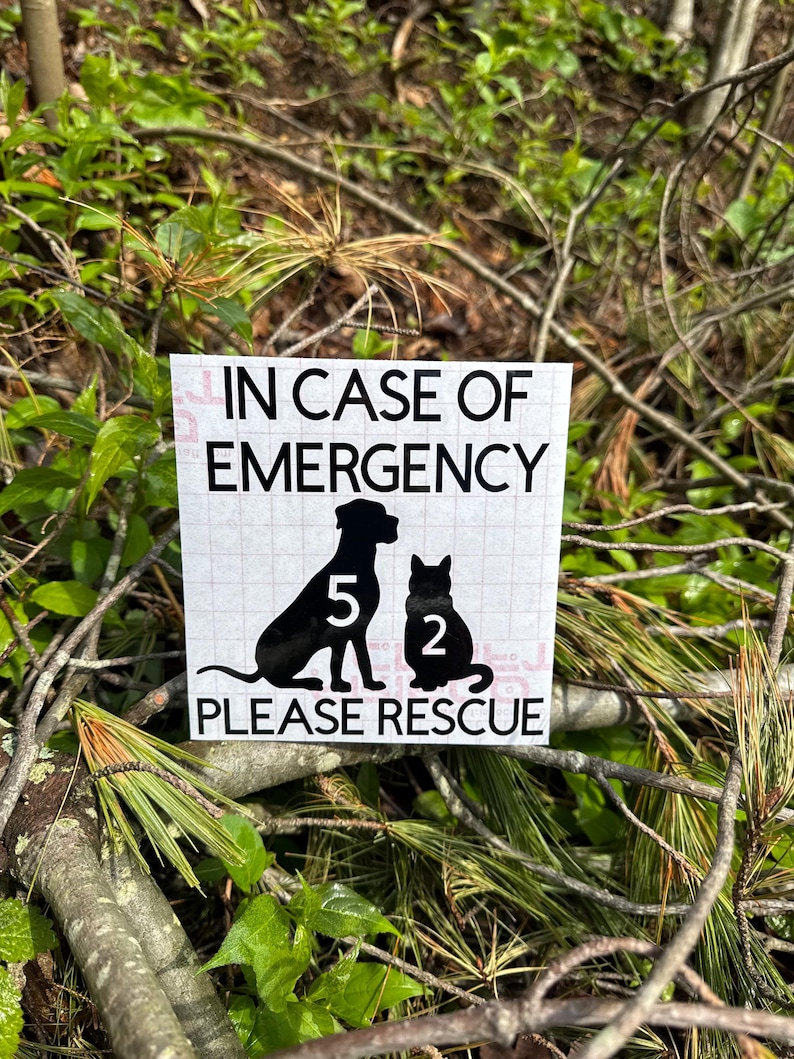 May include: A white square sign with the text "IN CASE OF EMERGENCY" above a black silhouette of a dog and cat. The dog has the number "5" and the cat has the number "2". The text "PLEASE RESCUE" is below the animals.
