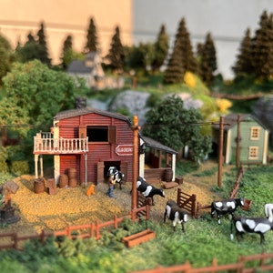 Pu&ograve; includere: Un modello in miniatura di una scena di fattoria con un fienile rosso con l'etichetta "Blacksmith", un piccolo cane e diverse mucche bianche e nere. La scena &egrave; ambientata in un campo erboso con una recinzione di legno e una piccola mangiatoia di legno.