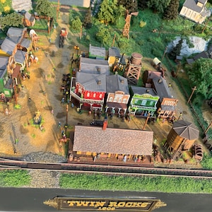 Pu&ograve; includere: Un modello in miniatura di una citt&agrave; western chiamata "Twin Rocks 1808" con edifici in legno, una torre d'acqua e un binario ferroviario. La citt&agrave; &egrave; circondata da alberi e rocce.