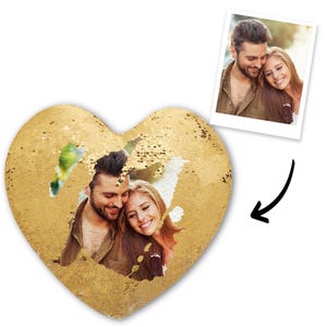 May include: A heart-shaped sequin pillow with a gold color. The pillow features a photo of a couple. A small photo of the couple is also included. The pillow is a decorative item.