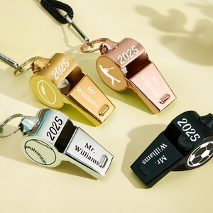 May include: Four metal whistles in gold, rose gold, and silver, and black. Each whistle has the year "2025" and the name "Mr. Williams" engraved. The whistles feature sports-themed designs: football, baseball, soccer, and a baseball player.