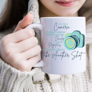Puede incluir: Taza de cerámica blanca con un gráfico de cámara azul y amarillo y el texto "La vida es como una cámara. Concéntrate en lo importante. Captura los buenos momentos. Desarrolla los negativos de la y si las cosas no funcionan, toma otra foto."