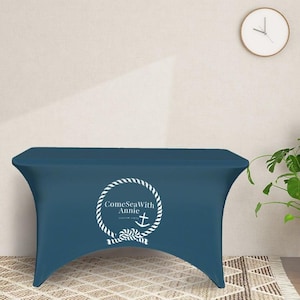 May include: A dark blue fitted table cover with a white rope circle design and the text "ComeSeaWith Annie" and an anchor symbol.