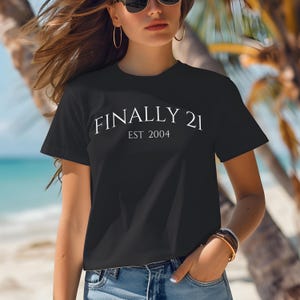 May include: A black t-shirt with white text that reads "FINALLY 21 EST 2004".