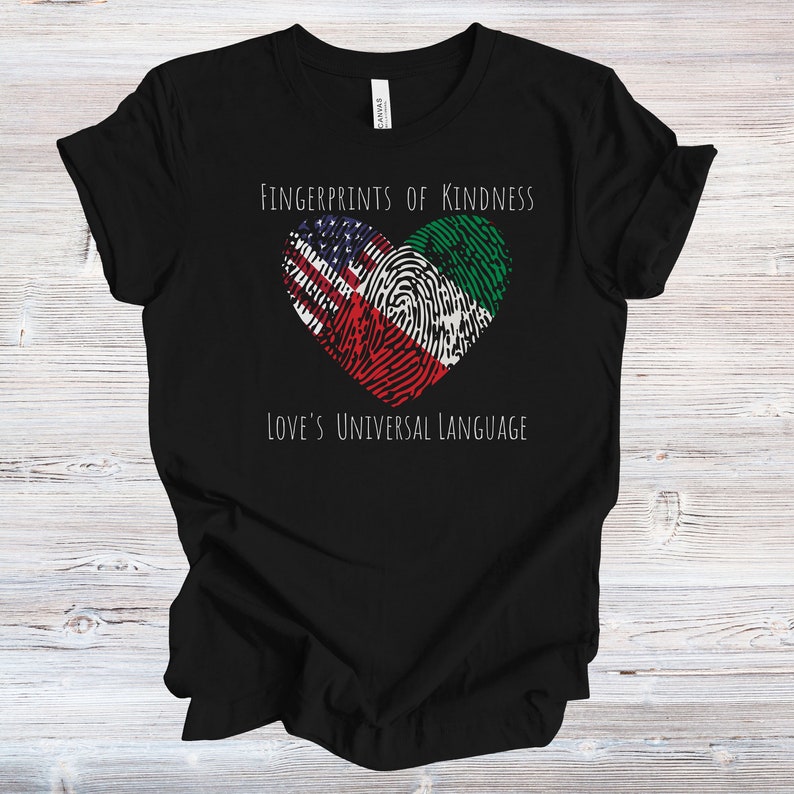May include: Black t-shirt with a white heart-shaped fingerprint design. The fingerprint is made up of the American and Nigerian flags. The text "Fingerprints of Kindness" and "Love's Universal Language" is printed in white on the shirt.