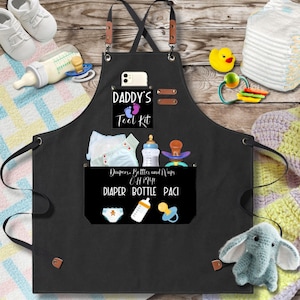 May include: Black canvas apron with a large pocket that says "Daddy's Tool Kit" and has a smaller pocket with the words "Diapers, Bottles and Naps OH MY! DIAPER BOTTLE PACI".