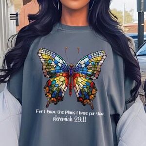 Puede incluir: Una sudadera gris con un diseño de mariposa de vitral colorido y el texto "Porque yo sé los planes que tengo para vosotros Jeremías 29:11".