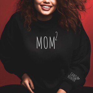 May include: Black sweatshirt with the text "MOM²" in white on the front and the text "GRACE HUNTER" with a heart symbol in white on the left sleeve.