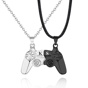 May include: A black and silver necklace with a pendant shaped like a video game controller. The pendant is split in half, with one side black and the other silver. The letters "K" and "S" are engraved on the pendant.