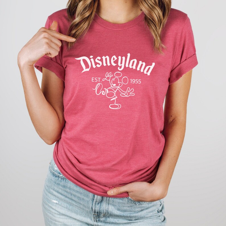 May include: A pink t-shirt with a white outline of Mickey Mouse and the text "Disneyland EST. 1955".